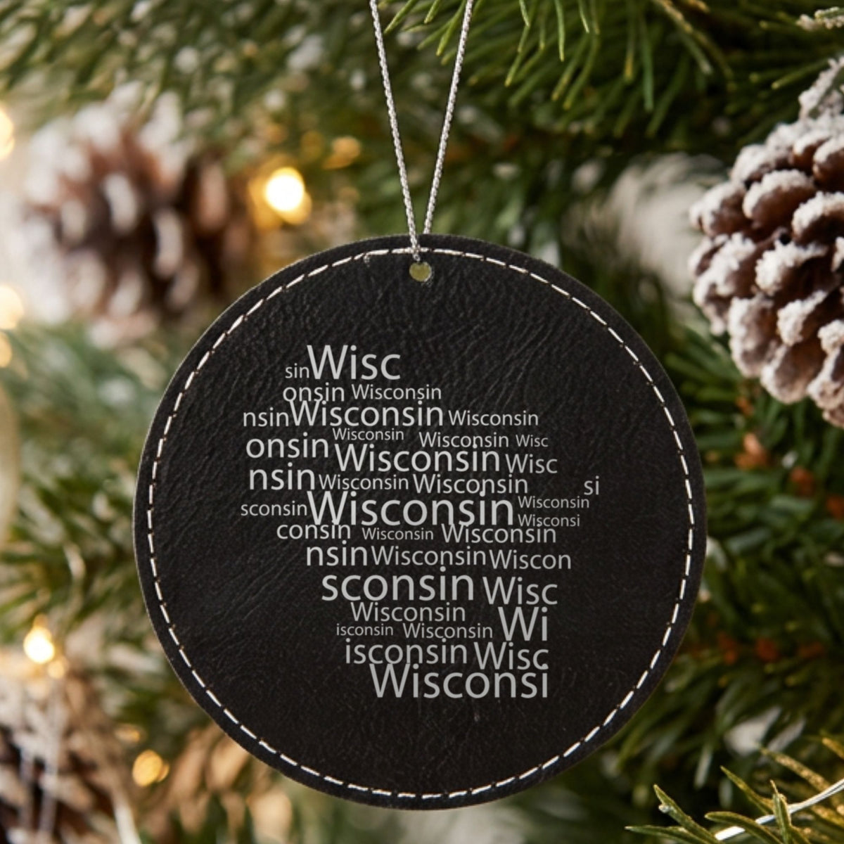 Black leatherette round Christmas ornament laser engraved with the Wisconsin Word Cloud design, hanging on a tree