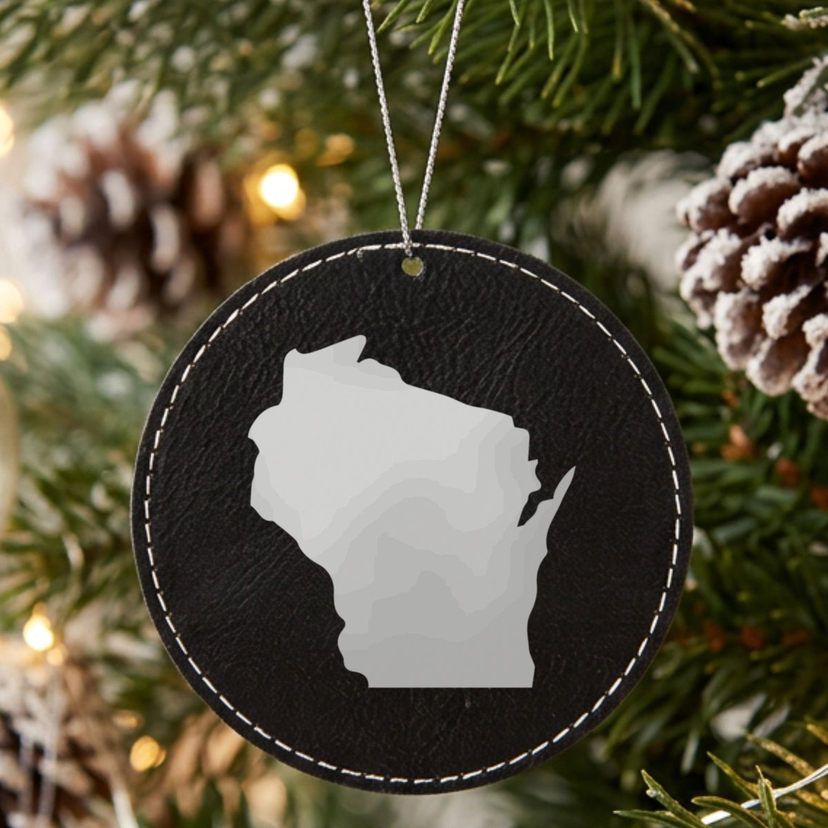 Black leatherette round Christmas ornament laser engraved with the Wisconsin Engraved State design, hanging on a tree