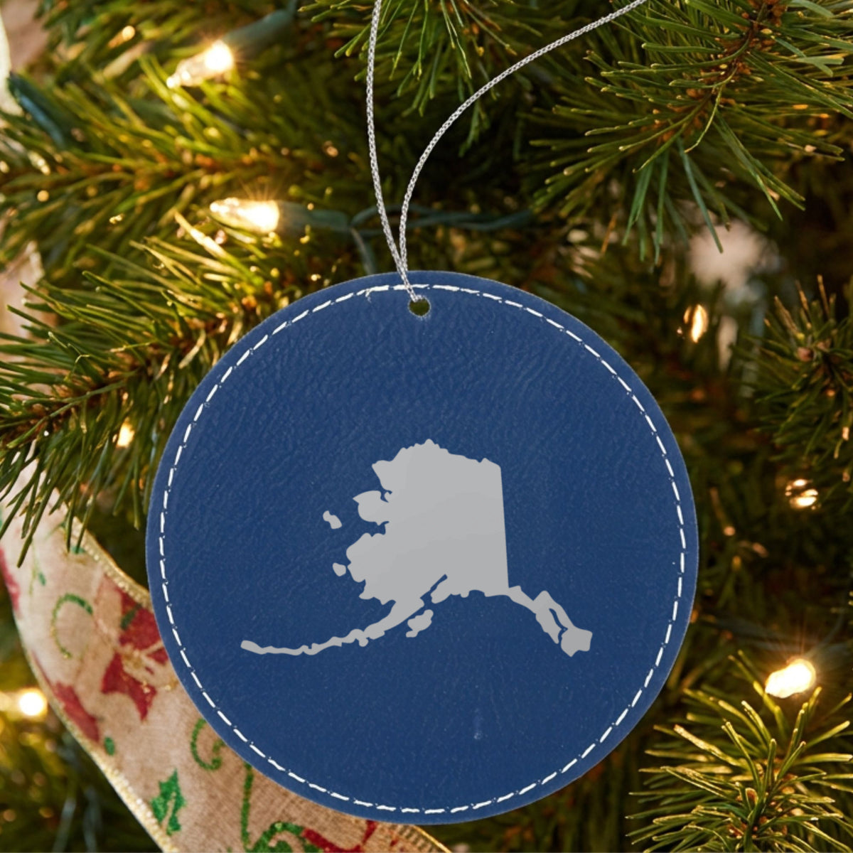 Blue leatherette round Christmas ornament laser engraved with the Alaska Engraved State design, hanging on a tree