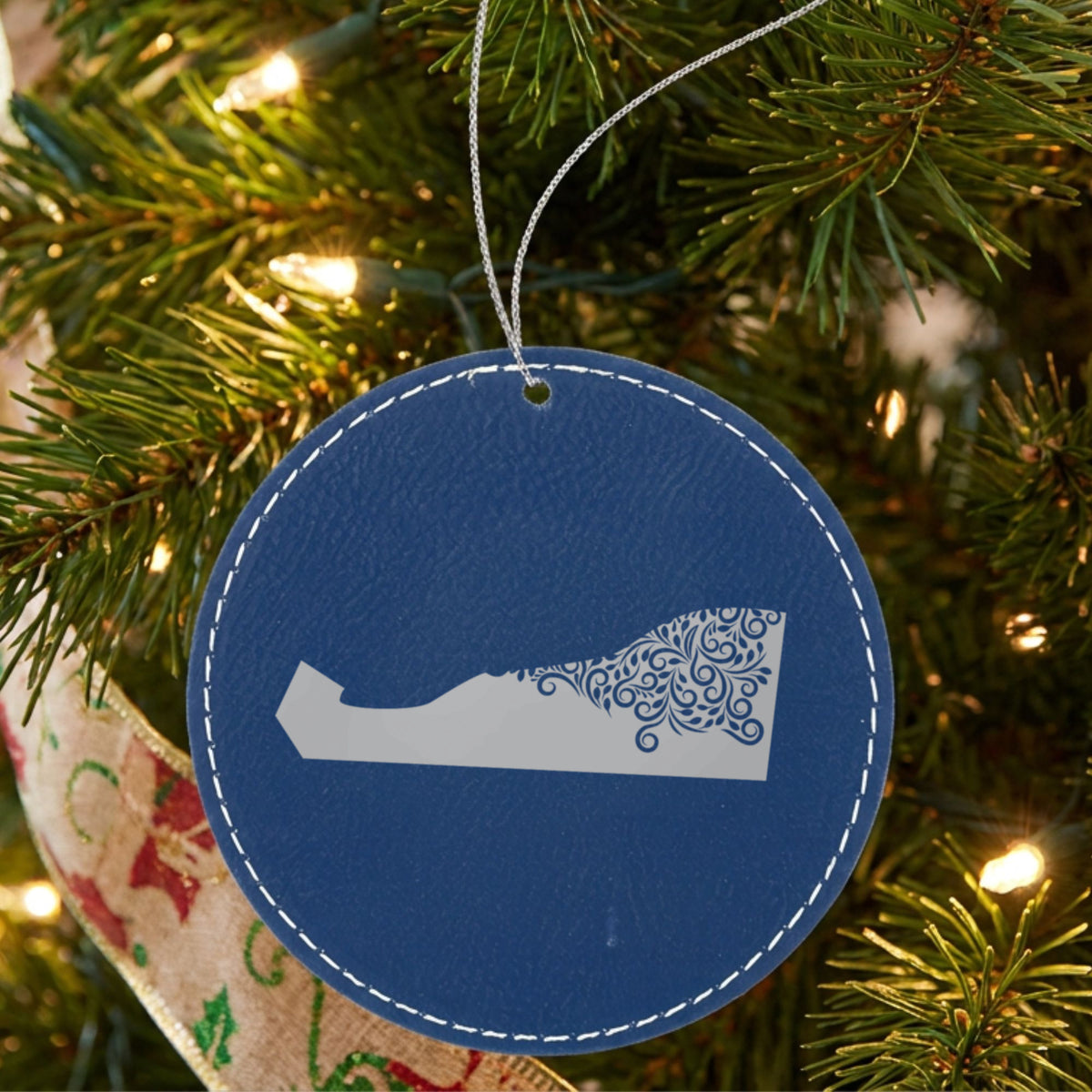 Blue leatherette round Christmas ornament laser engraved with the Delaware Floral Damask design, hanging on a tree
