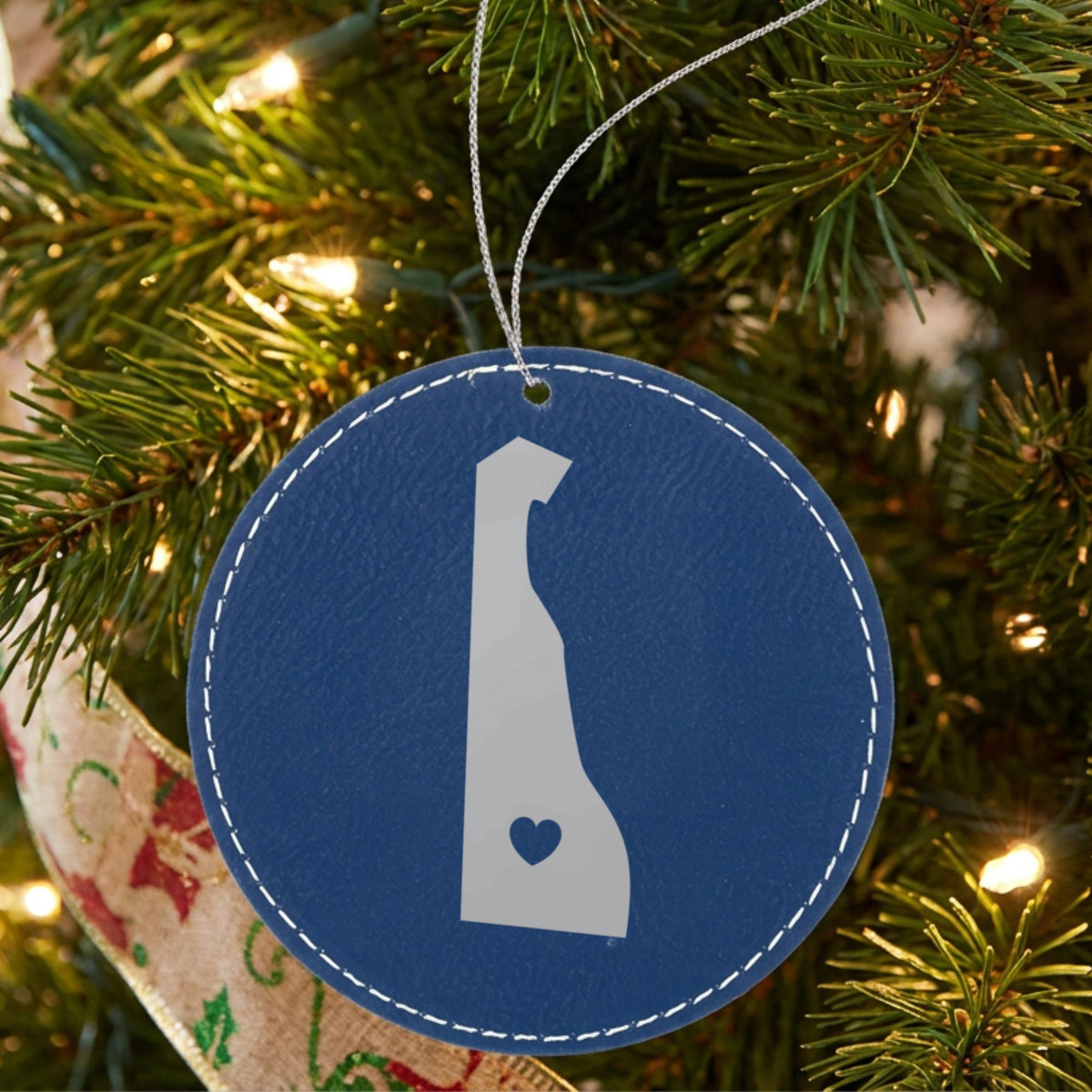 Blue leatherette round Christmas ornament laser engraved with the Delaware Heart Accent design, hanging on a tree
