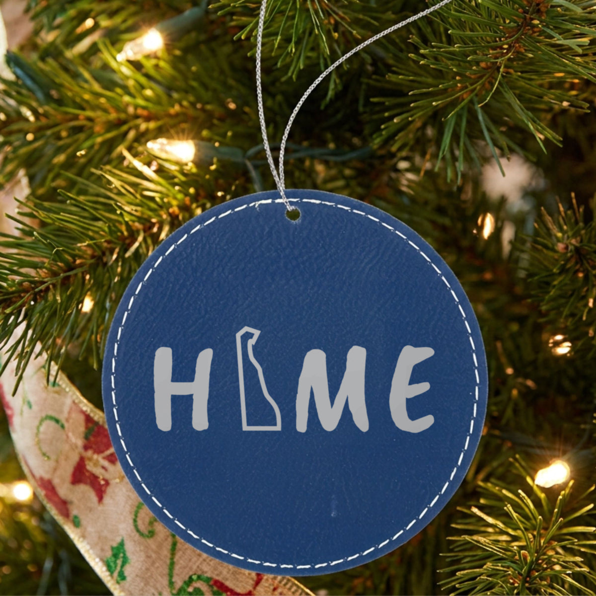 Blue leatherette round Christmas ornament laser engraved with the Delaware HOME Outline design, hanging on a tree