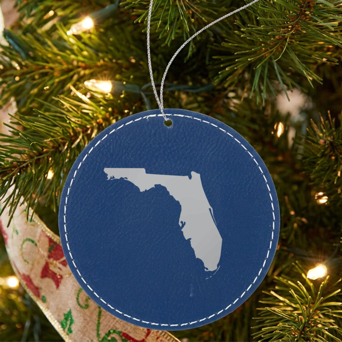 Blue leatherette round Christmas ornament laser engraved with the Florida Engraved State design, hanging on a tree