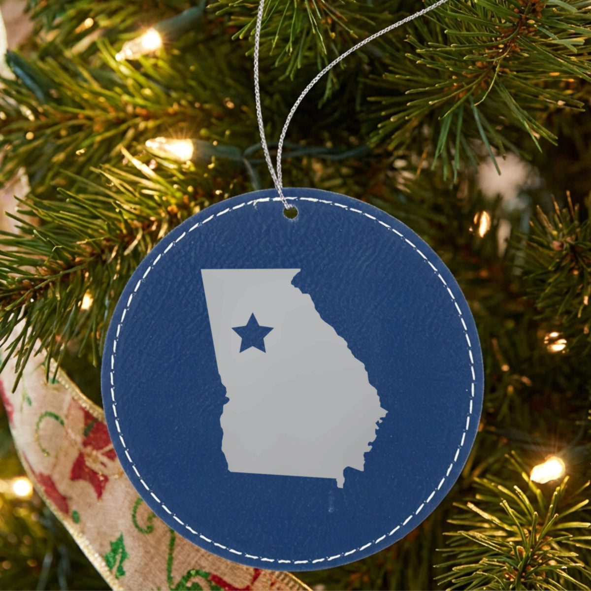 Blue leatherette round Christmas ornament laser engraved with the Georgia Star Accent design, hanging on a tree
