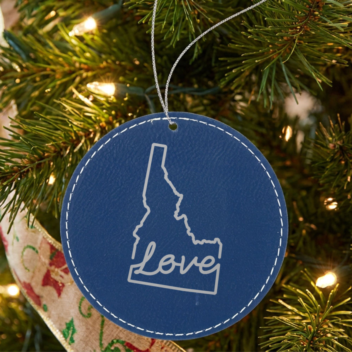 Blue leatherette round Christmas ornament laser engraved with the Idaho Hand-Drawn Love design, hanging on a tree