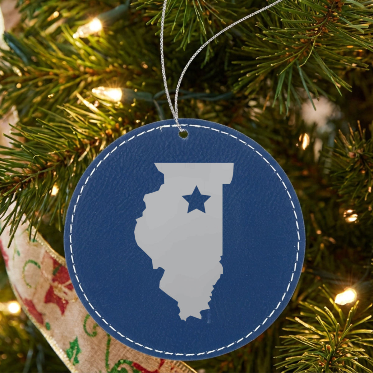 Blue leatherette round Christmas ornament laser engraved with the Illinois Star Accent design, hanging on a tree