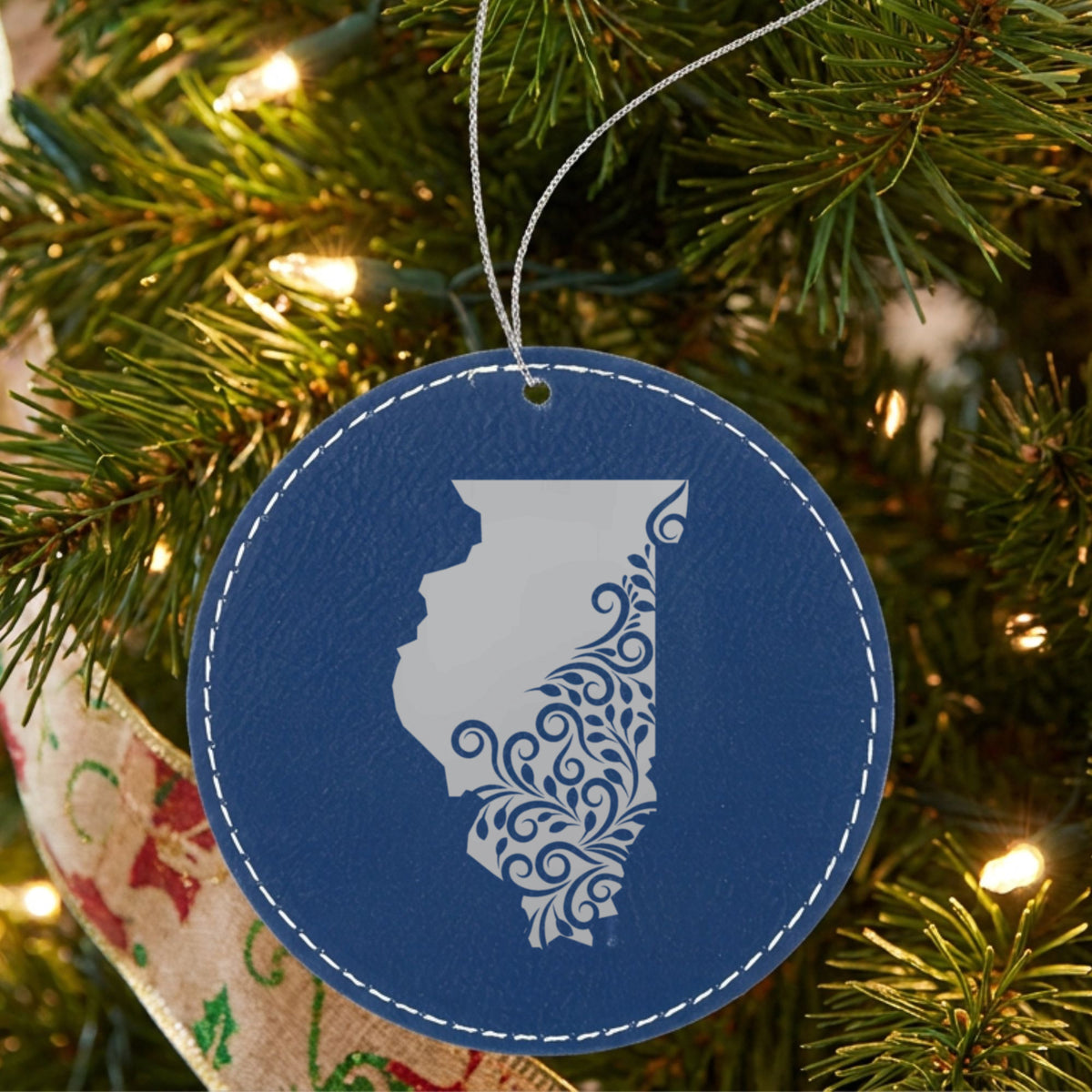 Blue leatherette round Christmas ornament laser engraved with the Illinois Floral Damask design, hanging on a tree