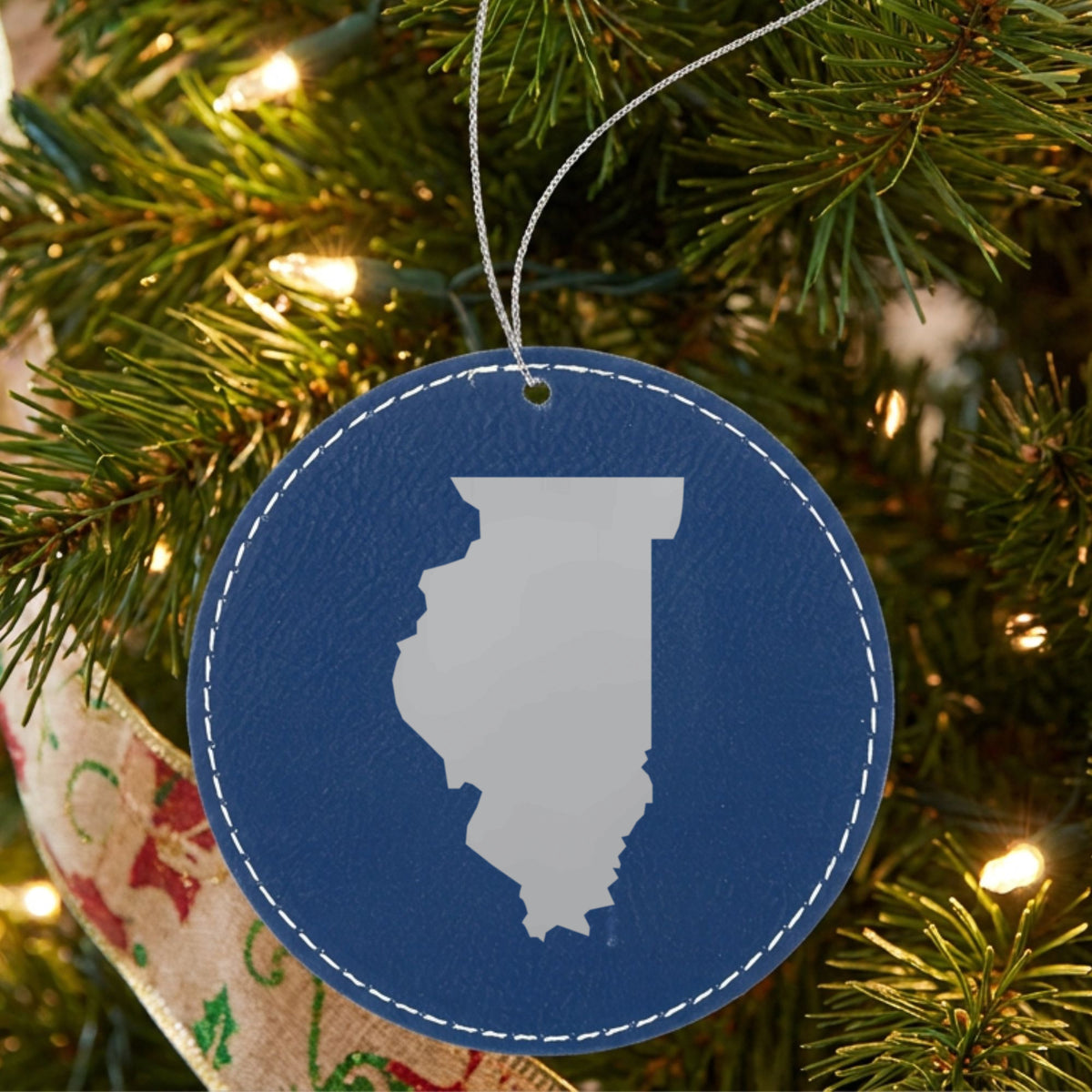 Blue leatherette round Christmas ornament laser engraved with the Illinois Engraved State design, hanging on a tree