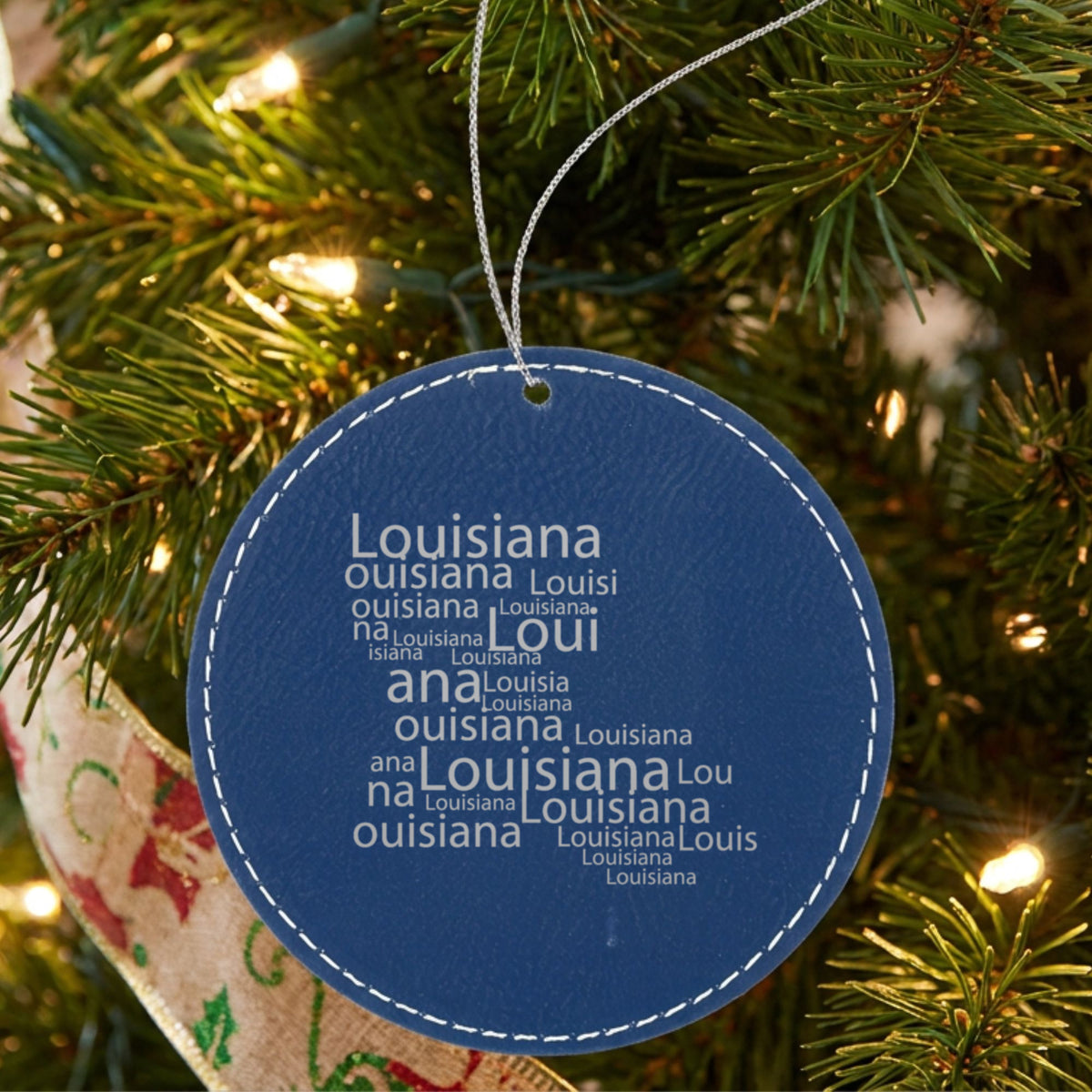 Blue leatherette round Christmas ornament laser engraved with the Louisiana Word Cloud design, hanging on a tree