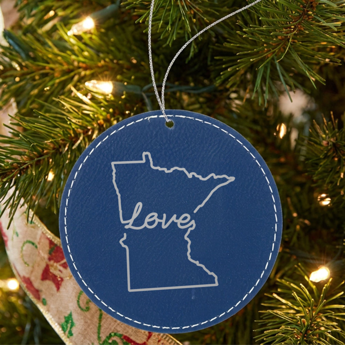 Blue leatherette round Christmas ornament laser engraved with the Minnesota Hand-Drawn Love design, hanging on a tree