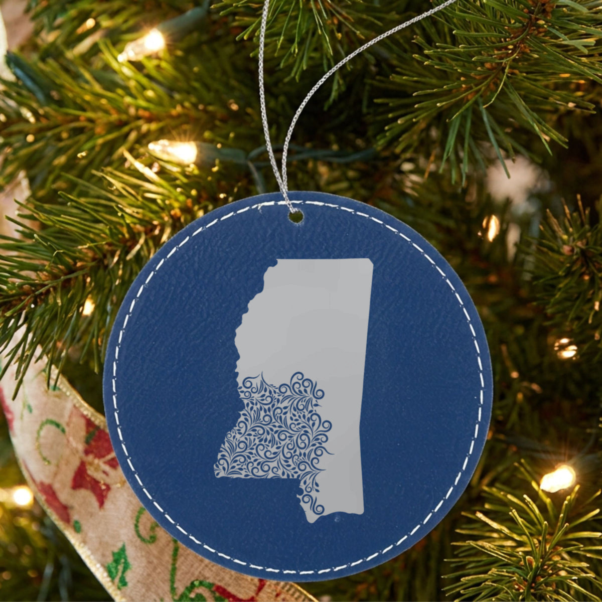 Blue leatherette round Christmas ornament laser engraved with the Mississippi Floral Damask design, hanging on a tree