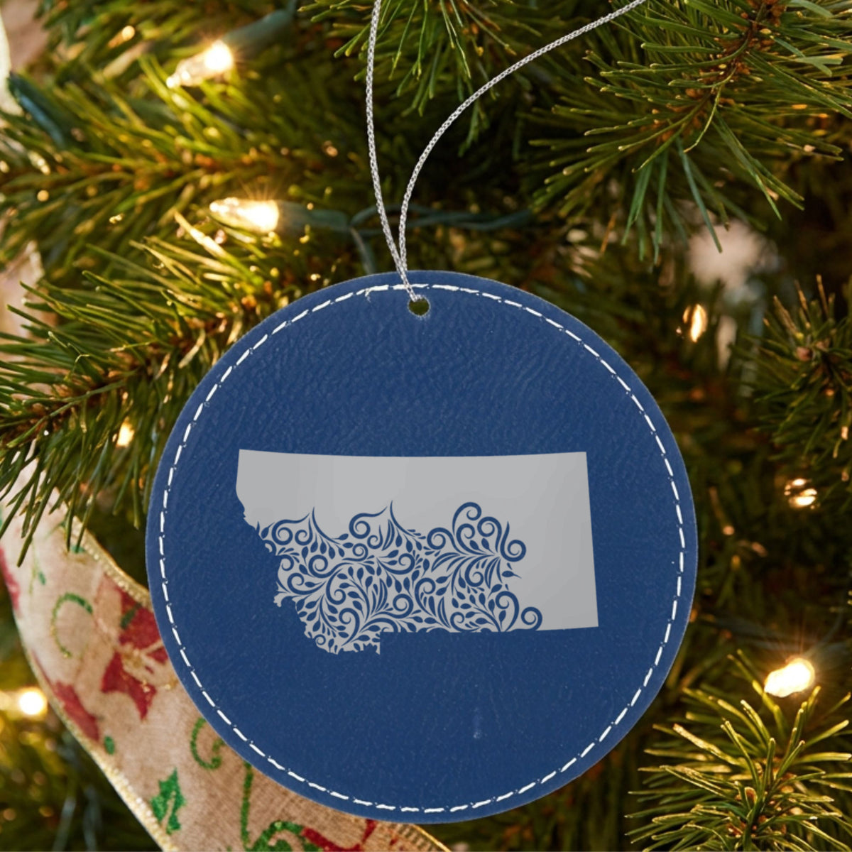 Blue leatherette round Christmas ornament laser engraved with the Montana Floral Damask design, hanging on a tree