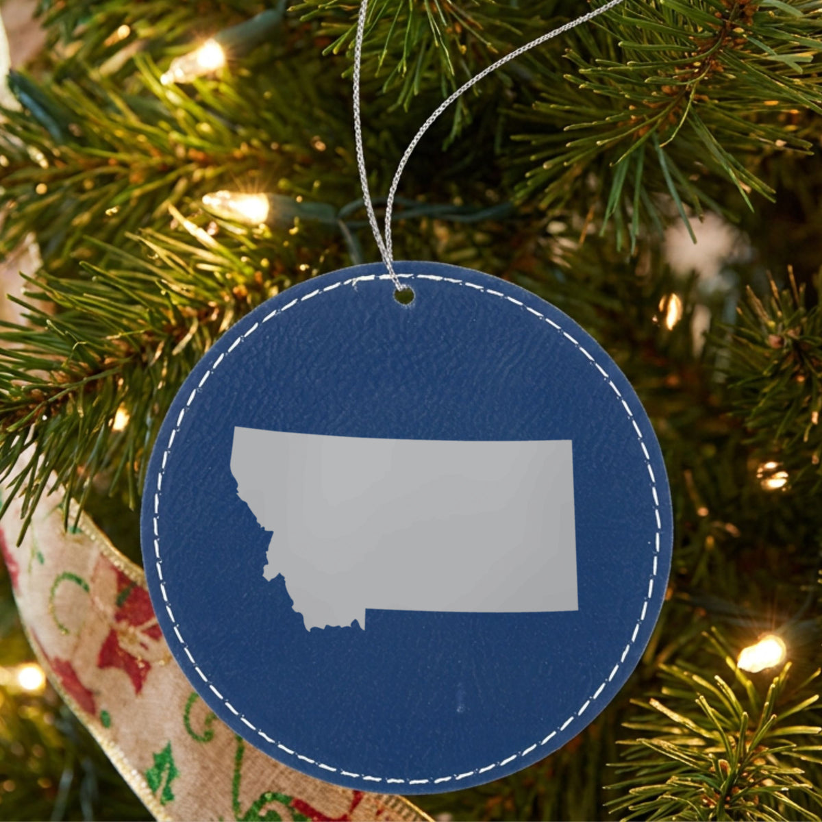 Blue leatherette round Christmas ornament laser engraved with the Montana Engraved State design, hanging on a tree