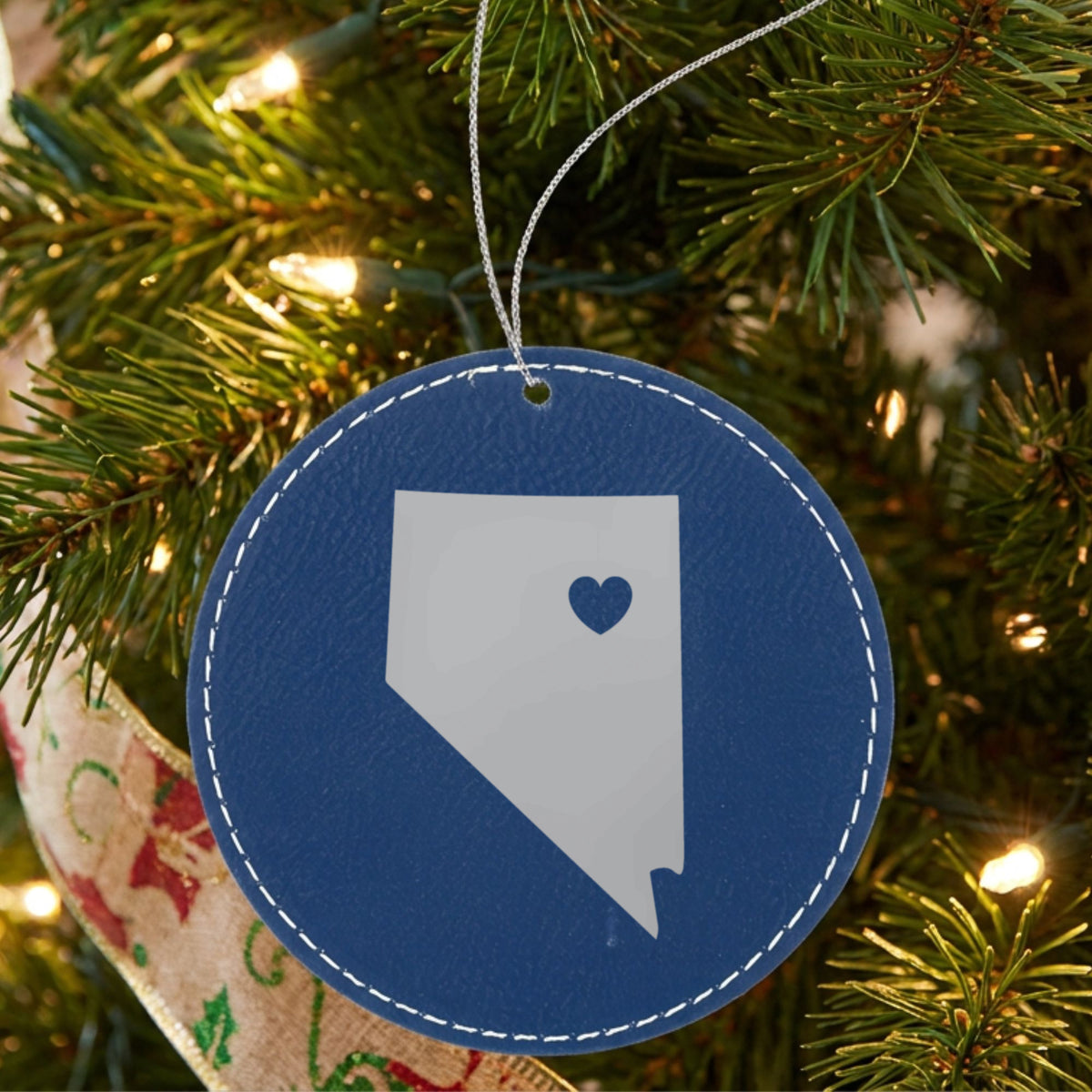 Blue leatherette round Christmas ornament laser engraved with the Nevada Heart Accent design, hanging on a tree