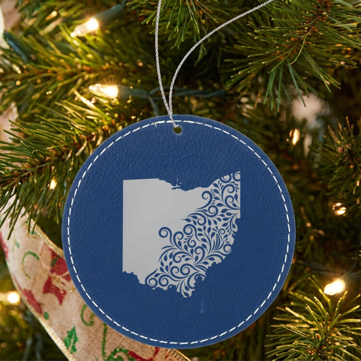 Blue leatherette round Christmas ornament laser engraved with the Ohio Floral Damask design, hanging on a tree