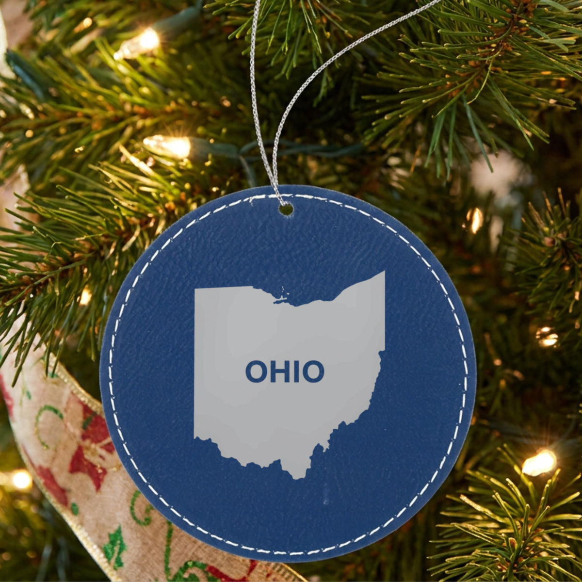 Blue leatherette round Christmas ornament laser engraved with the Ohio Bold State Name design, hanging on a tree
