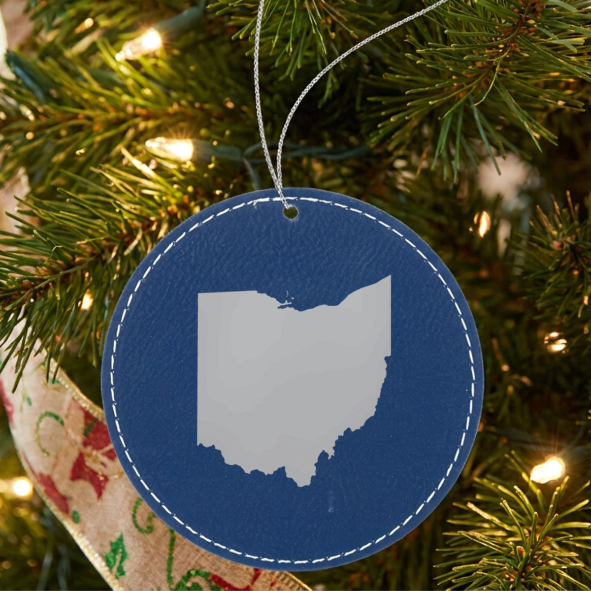 Blue leatherette round Christmas ornament laser engraved with the Ohio Engraved State design, hanging on a tree