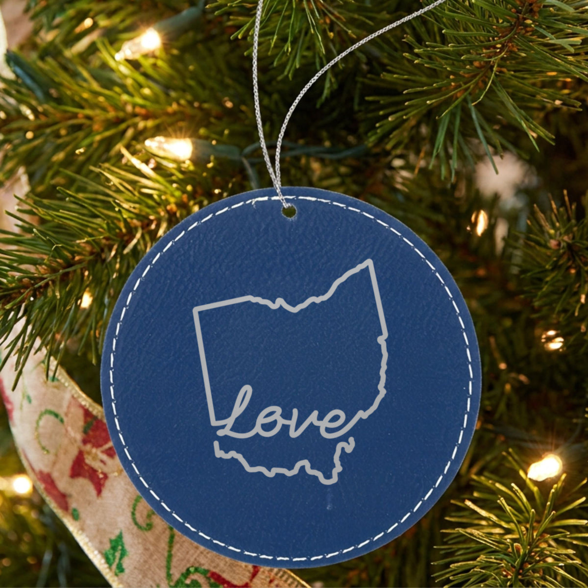 Blue leatherette round Christmas ornament laser engraved with the Ohio Hand-Drawn Love design, hanging on a tree