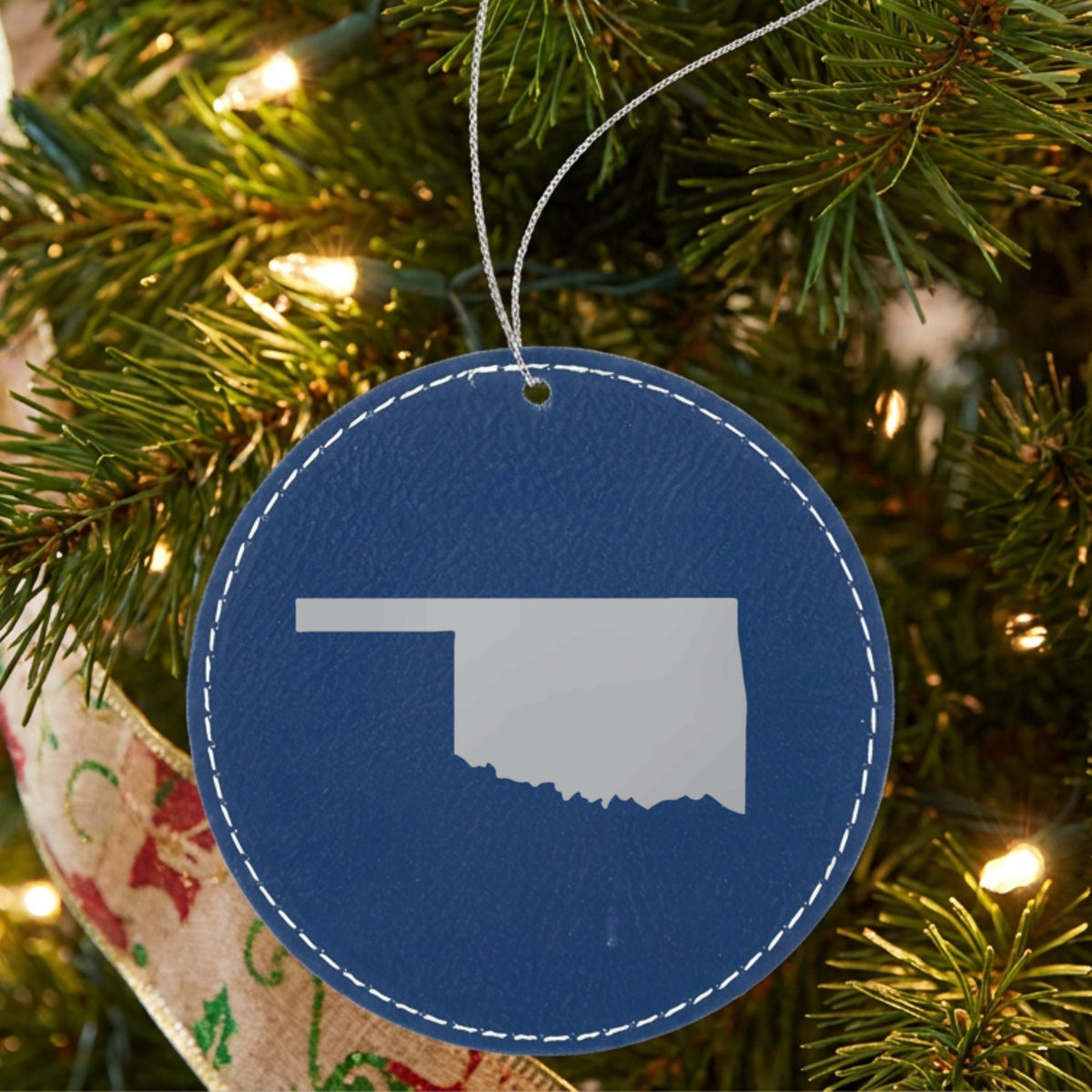 Blue leatherette round Christmas ornament laser engraved with the Oklahoma Engraved State design, hanging on a tree