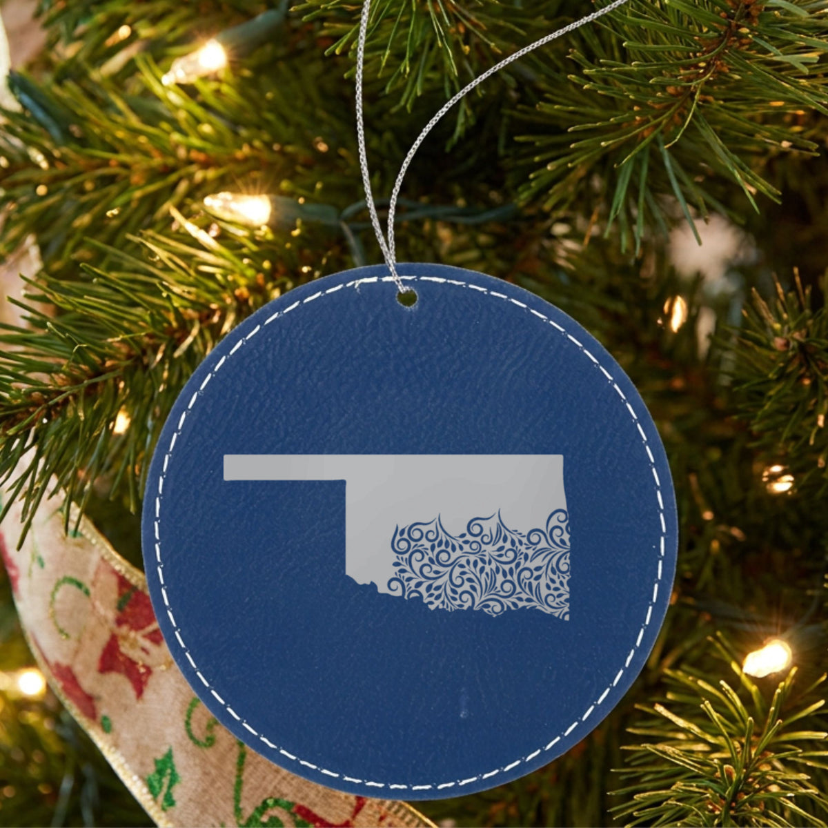Blue leatherette round Christmas ornament laser engraved with the Oklahoma Floral Damask design, hanging on a tree