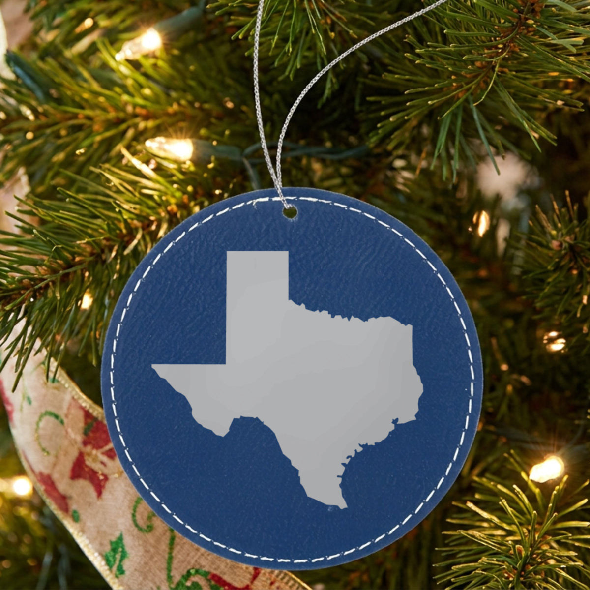Blue leatherette round Christmas ornament laser engraved with the Texas Engraved State design, hanging on a tree