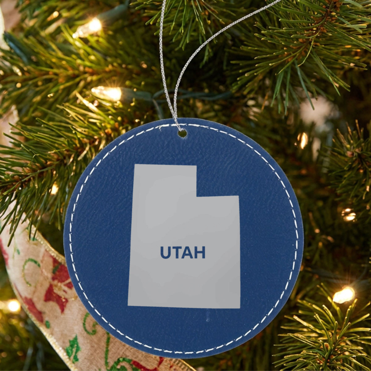 Blue leatherette round Christmas ornament laser engraved with the Utah Bold State Name design, hanging on a tree