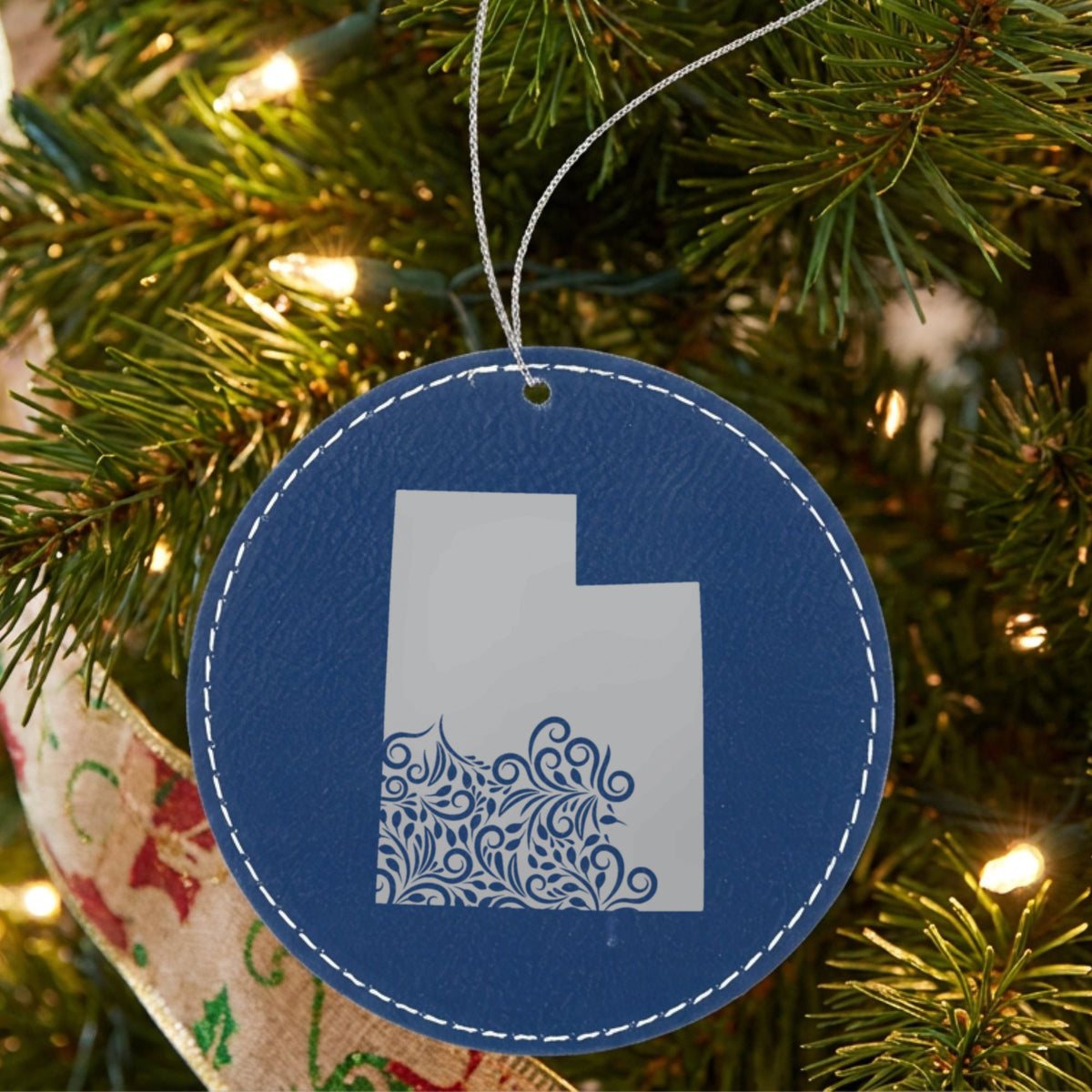 Blue leatherette round Christmas ornament laser engraved with the Utah Floral Damask design, hanging on a tree