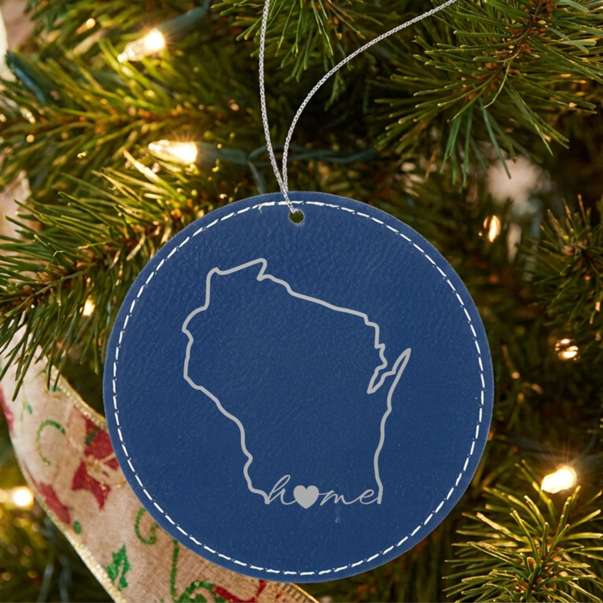Blue leatherette round Christmas ornament laser engraved with the Wisconsin Home Script & Heart design, hanging on a tree