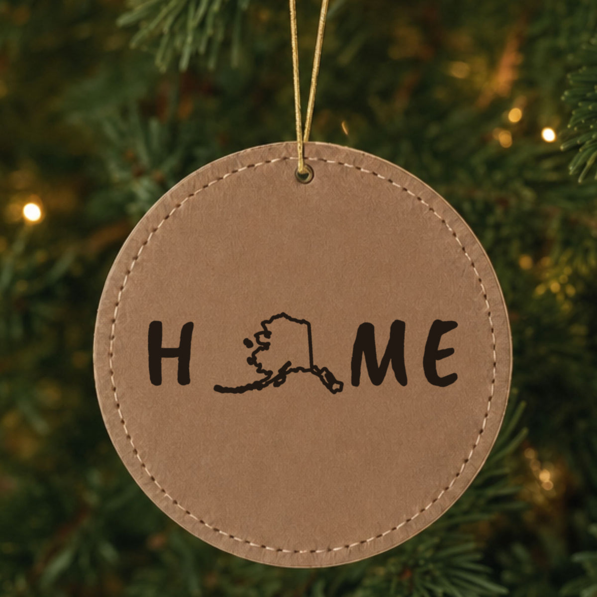 Brown leatherette round Christmas ornament laser engraved with the Alaska HOME Outline design, hanging on a tree