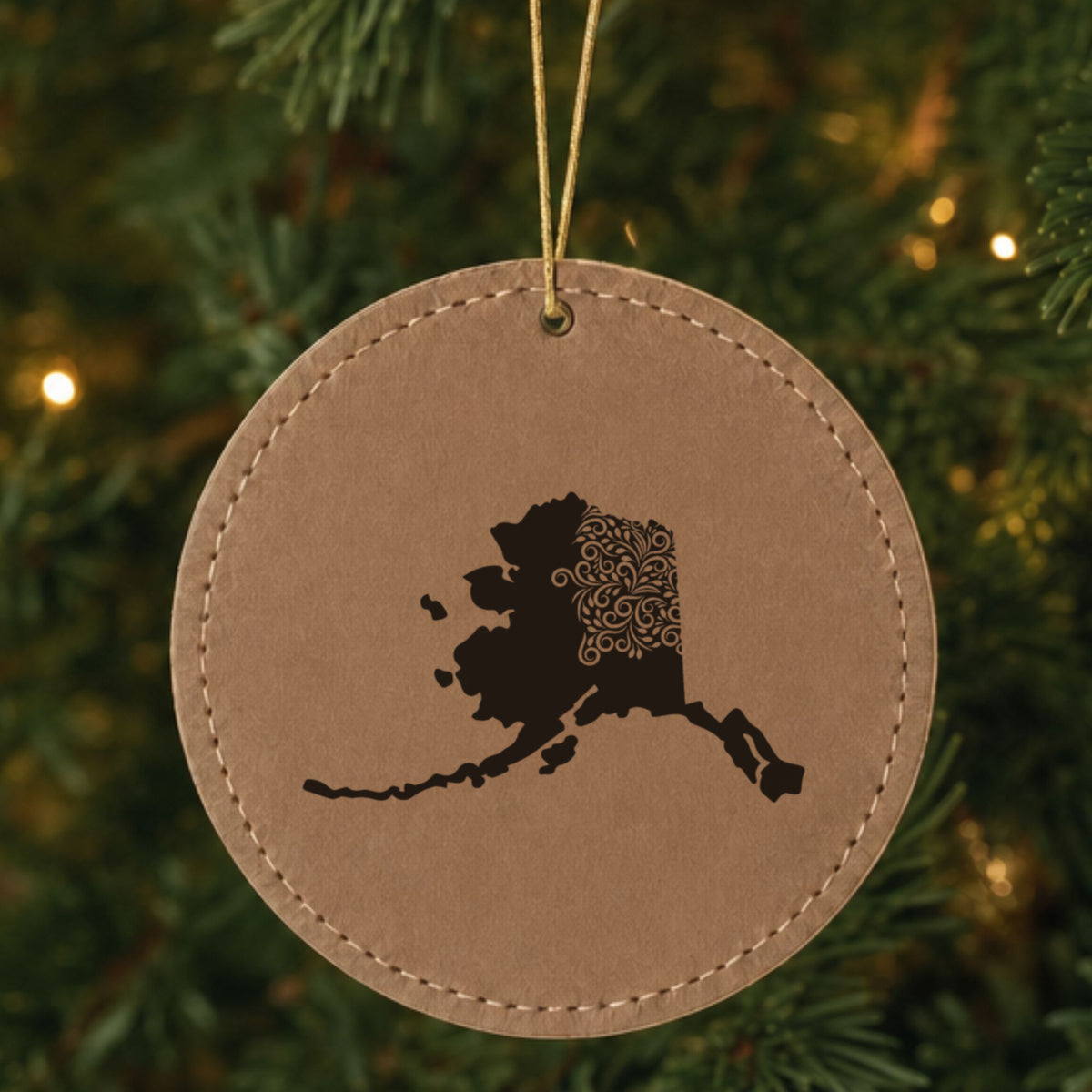Brown leatherette round Christmas ornament laser engraved with the Alaska Floral Damask design, hanging on a tree