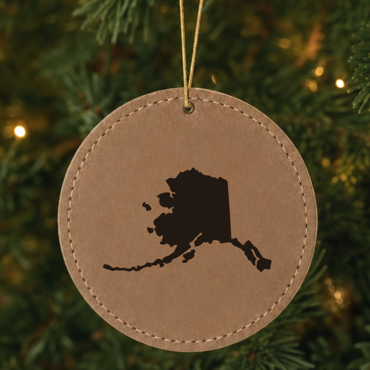 Brown leatherette round Christmas ornament laser engraved with the Alaska Engraved State design, hanging on a tree
