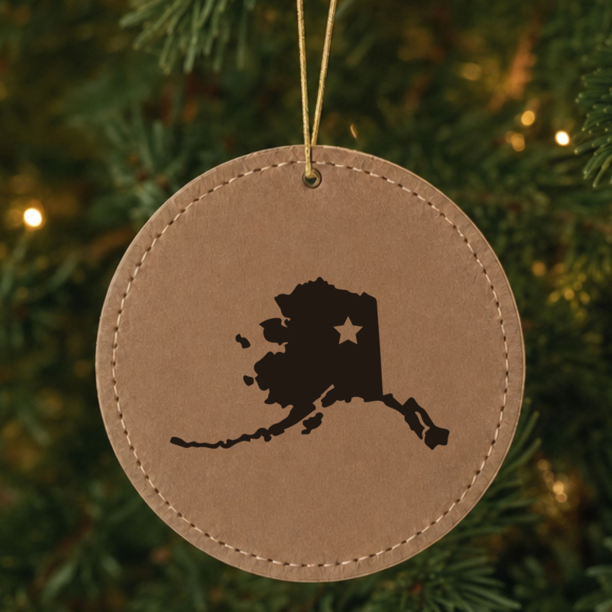 Brown leatherette round Christmas ornament laser engraved with the Alaska Star Accent design, hanging on a tree