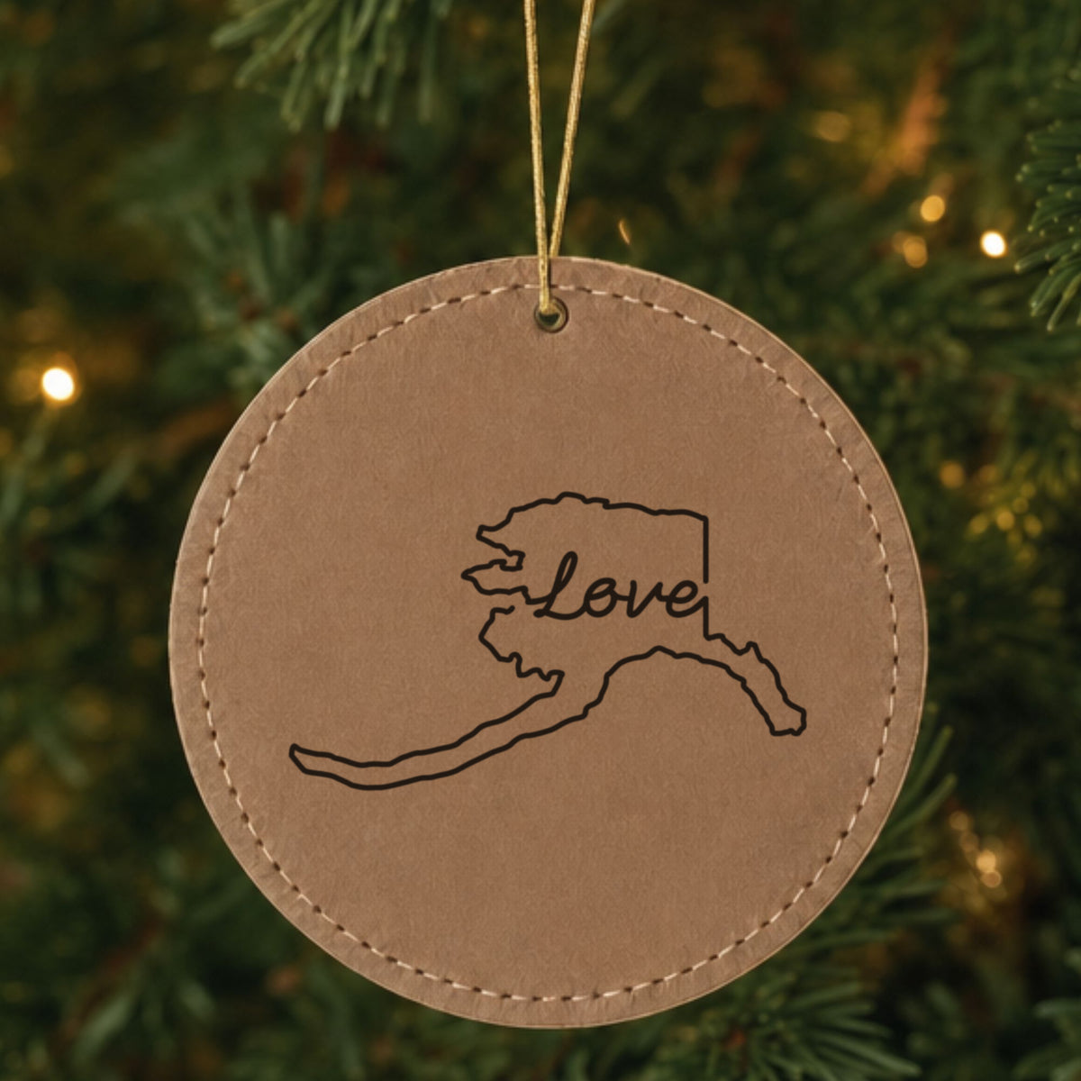 Brown leatherette round Christmas ornament laser engraved with the Alaska Hand-Drawn Love design, hanging on a tree