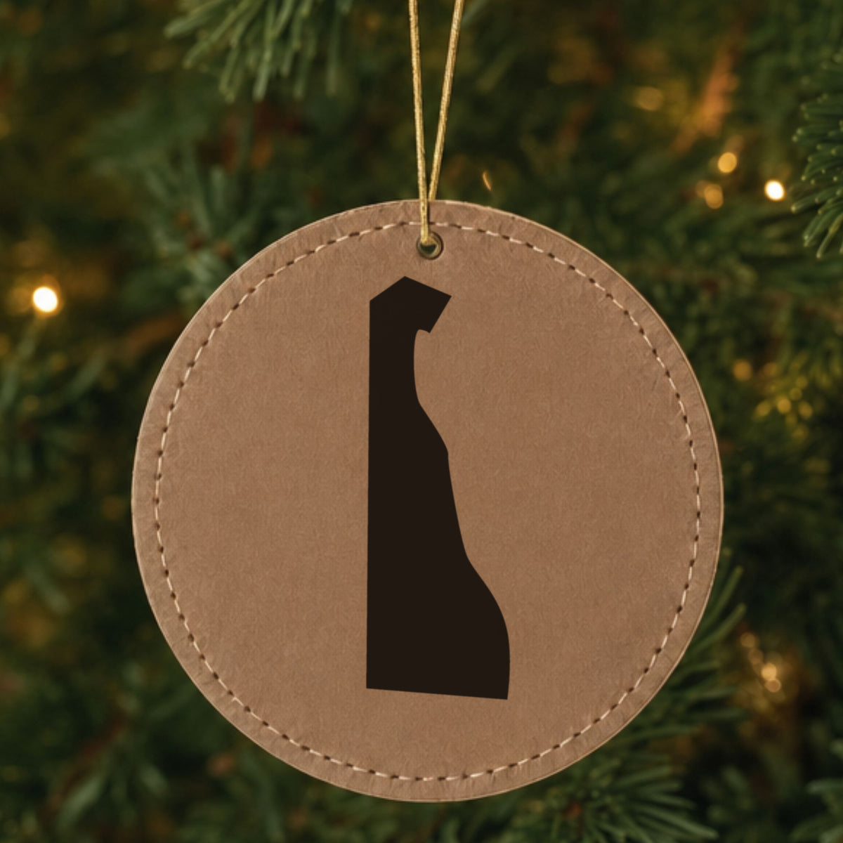 Brown leatherette round Christmas ornament laser engraved with the Delaware Engraved State design, hanging on a tree