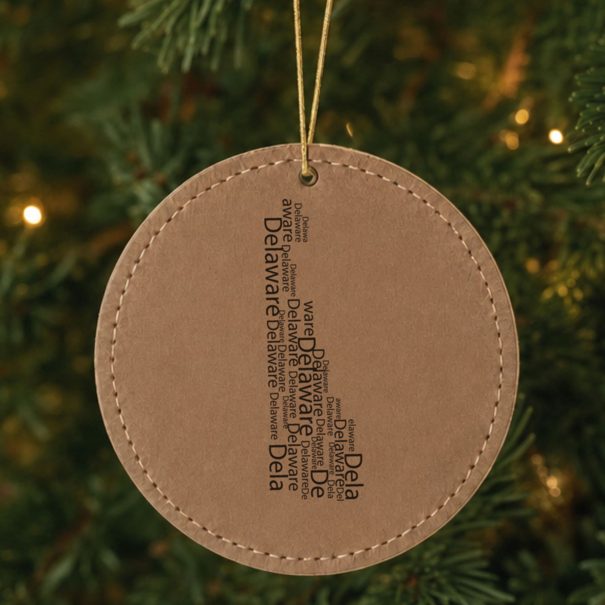 Brown leatherette round Christmas ornament laser engraved with the Delaware Word Cloud design, hanging on a tree