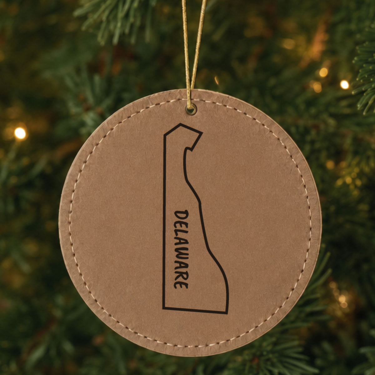 Brown leatherette round Christmas ornament laser engraved with the Delaware Vertical Name (Outline) design, hanging on a tree
