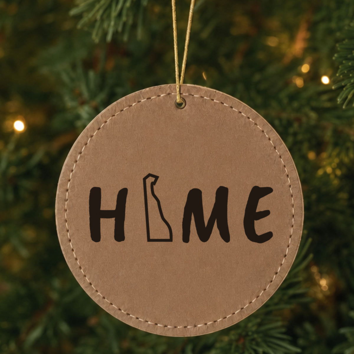 Brown leatherette round Christmas ornament laser engraved with the Delaware HOME Outline design, hanging on a tree