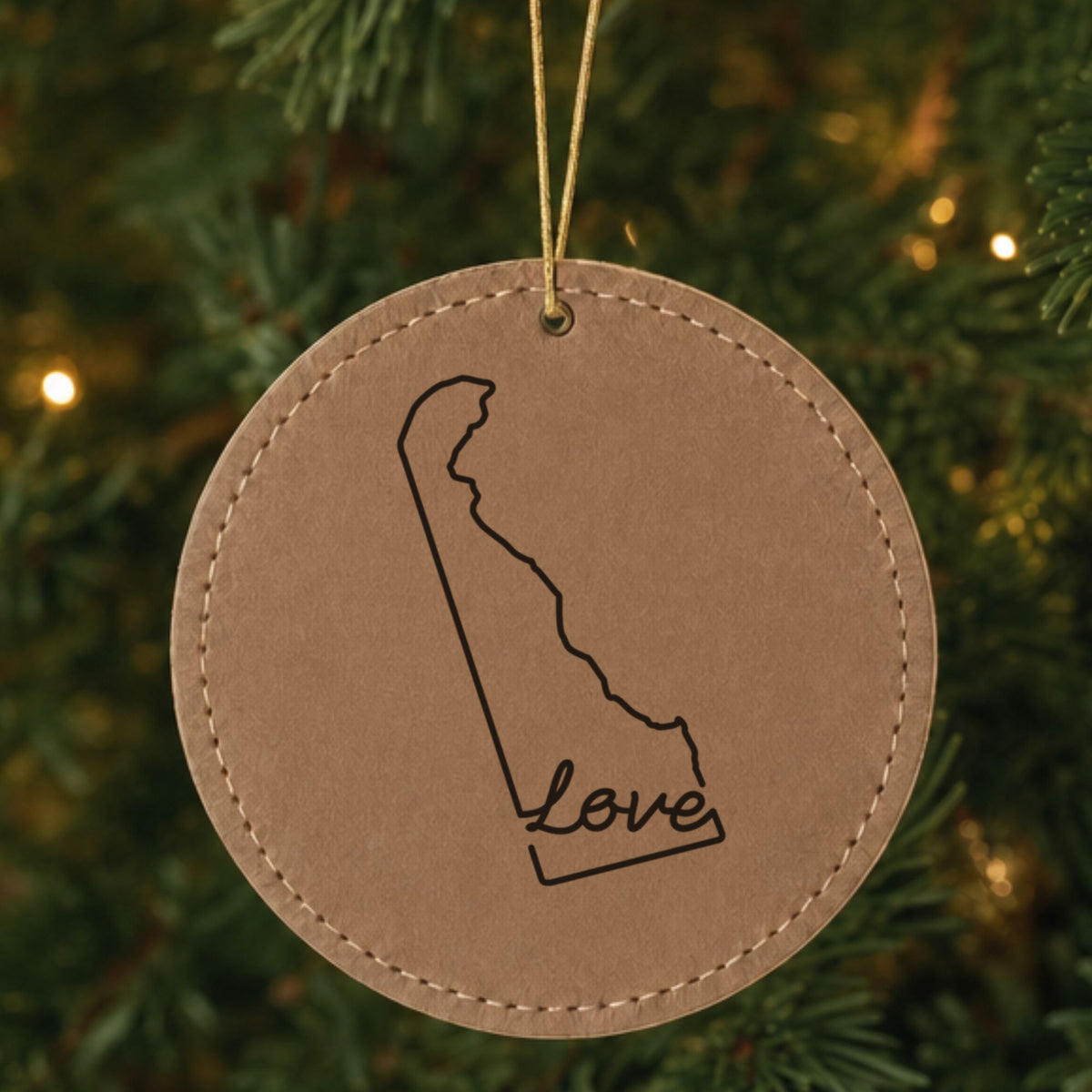 Brown leatherette round Christmas ornament laser engraved with the Delaware Hand-Drawn Love design, hanging on a tree