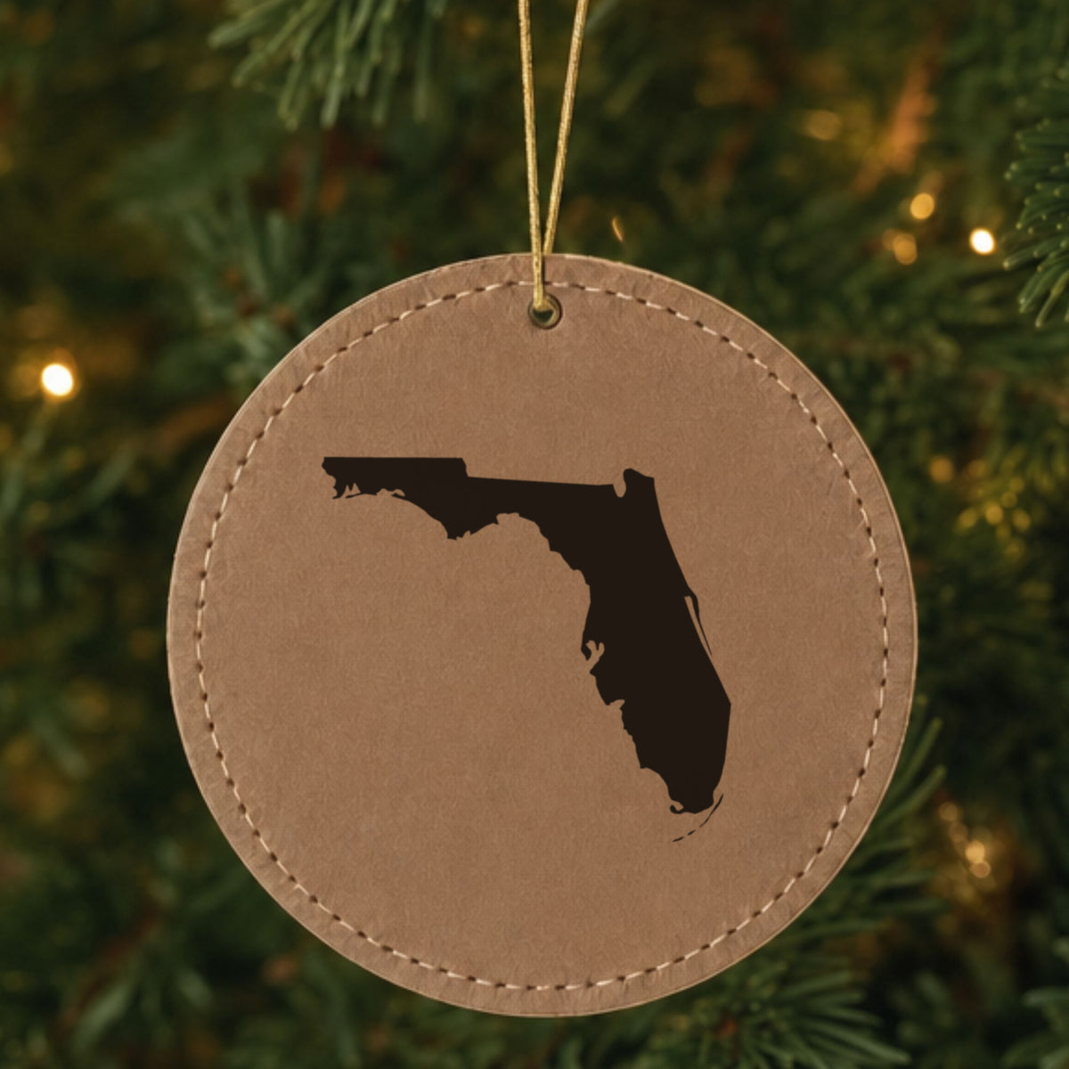 Brown leatherette round Christmas ornament laser engraved with the Florida Engraved State design, hanging on a tree