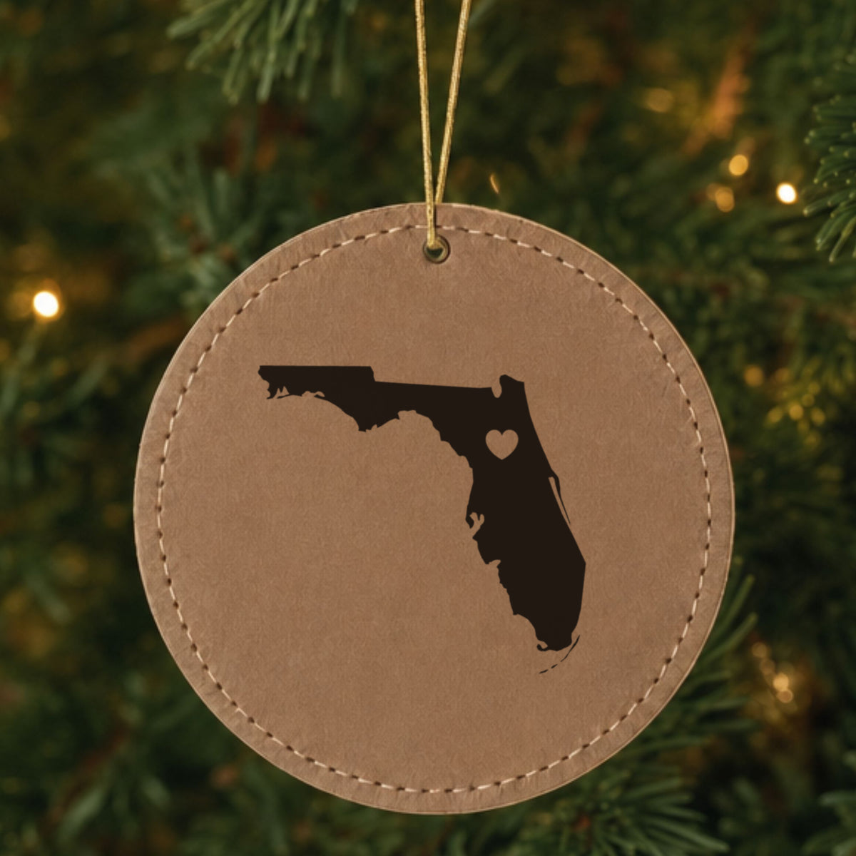 Brown leatherette round Christmas ornament laser engraved with the Florida Heart Accent design, hanging on a tree