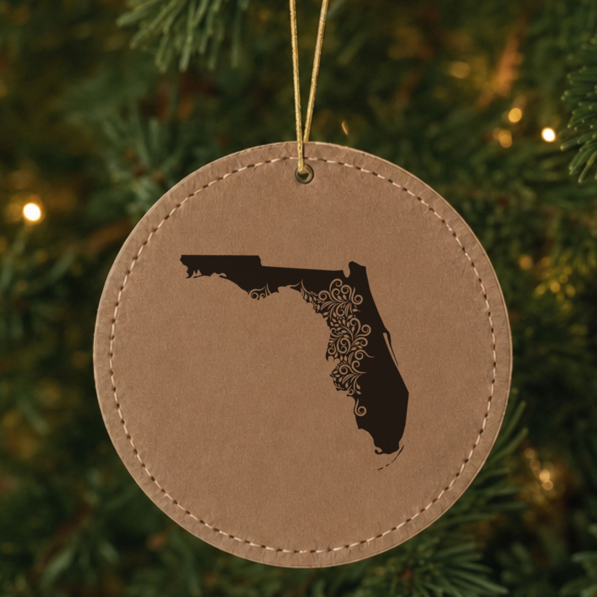 Brown leatherette round Christmas ornament laser engraved with the Florida Floral Damask design, hanging on a tree