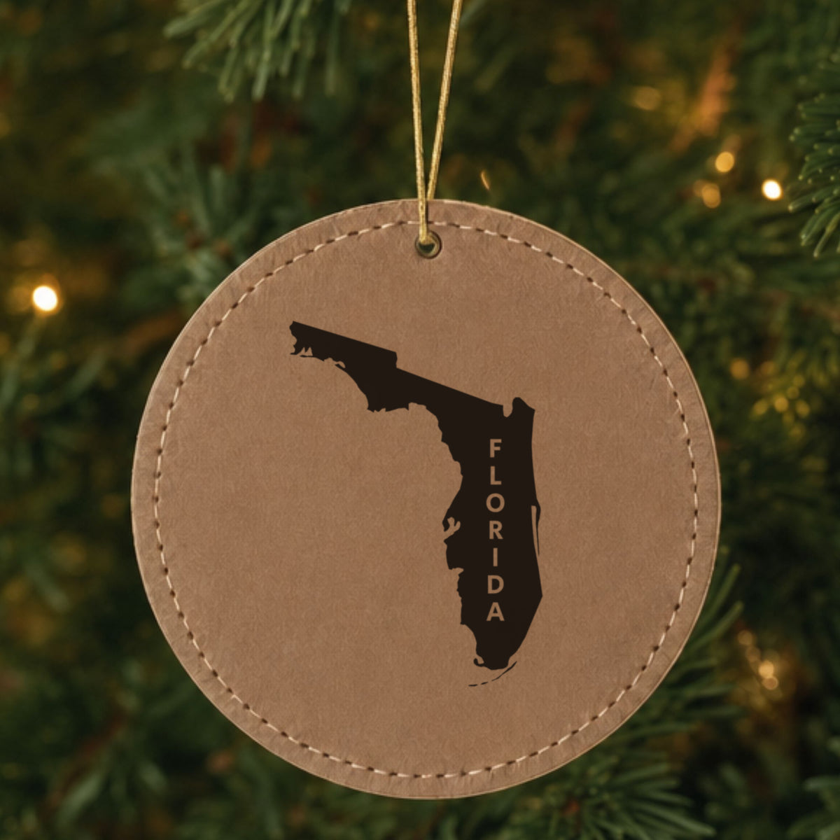 Brown leatherette round Christmas ornament laser engraved with the Florida Vertical Name (Engraved) design, hanging on a tree