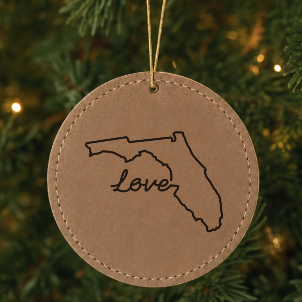 Brown leatherette round Christmas ornament laser engraved with the Florida Hand-Drawn Love design, hanging on a tree