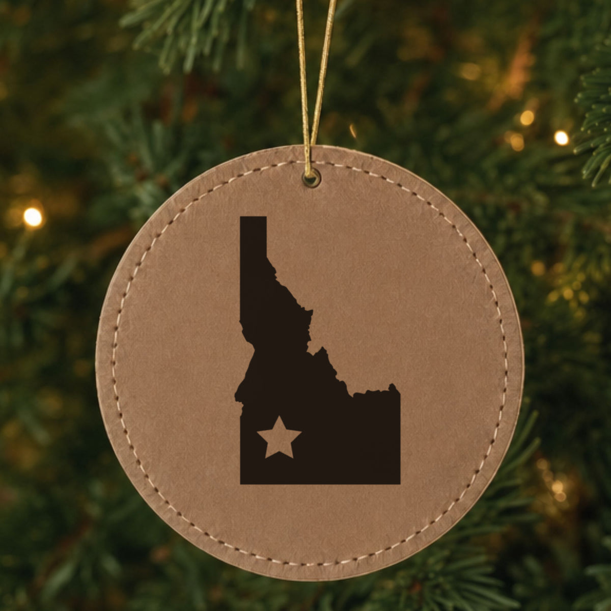 Brown leatherette round Christmas ornament laser engraved with the Idaho Star Accent design, hanging on a tree