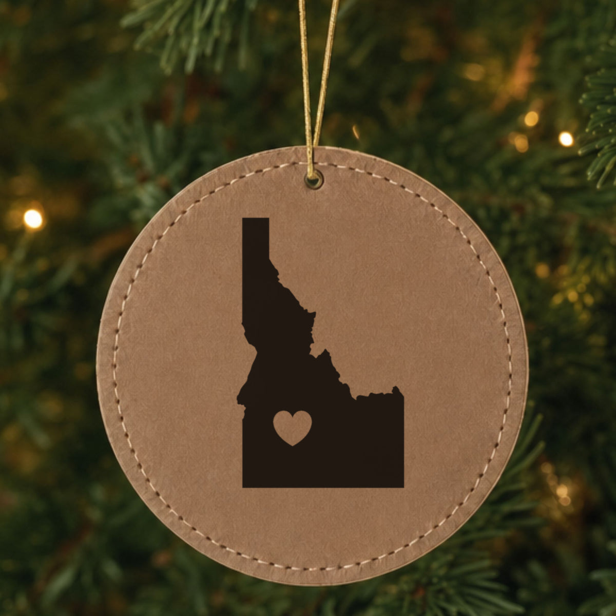 Brown leatherette round Christmas ornament laser engraved with the Idaho Heart Accent design, hanging on a tree