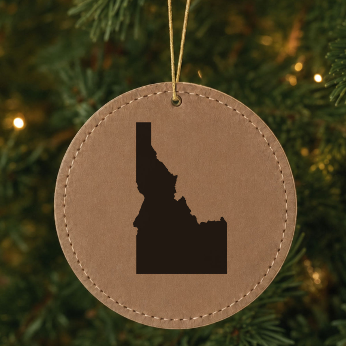 Brown leatherette round Christmas ornament laser engraved with the Idaho Engraved State design, hanging on a tree