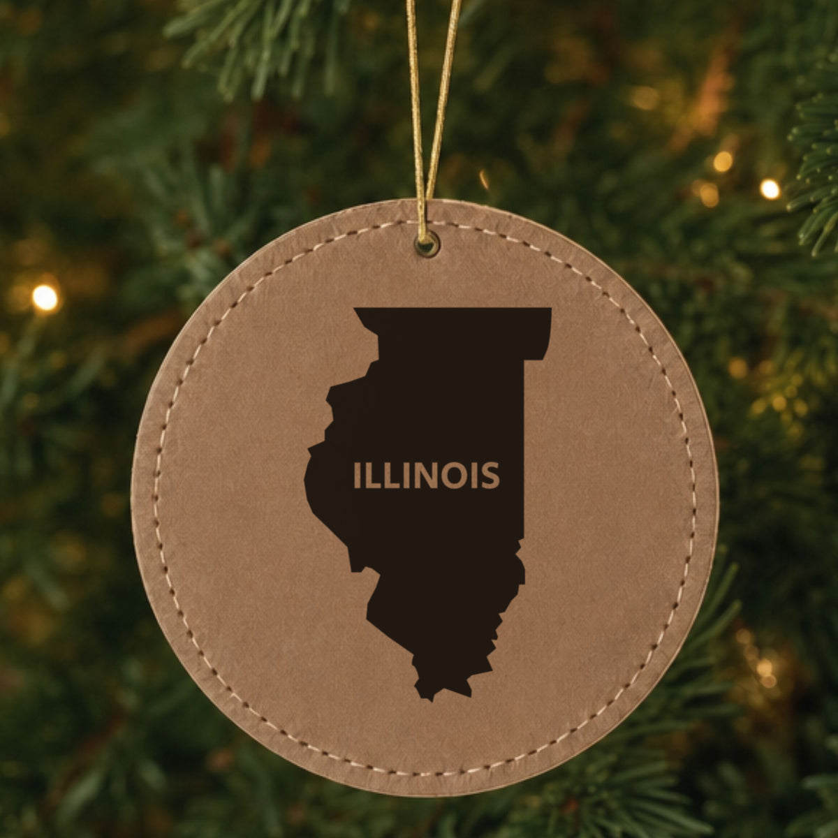 Brown leatherette round Christmas ornament laser engraved with the Illinois Bold State Name design, hanging on a tree