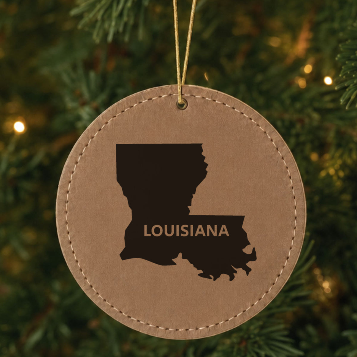 Brown leatherette round Christmas ornament laser engraved with the Louisiana Bold State Name design, hanging on a tree