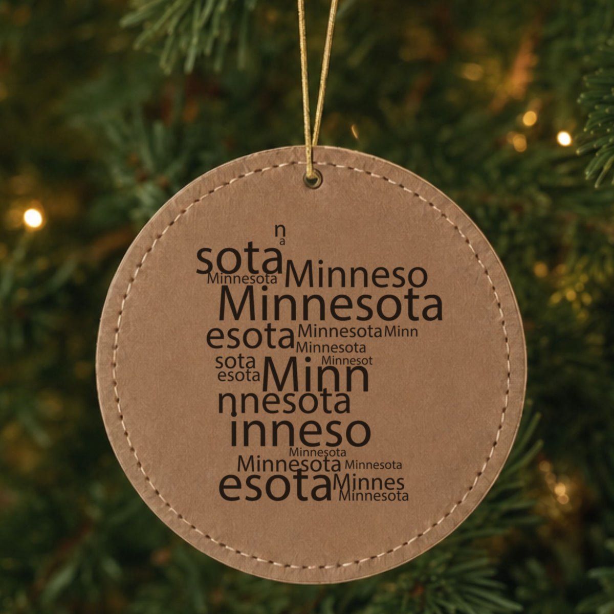 Brown leatherette round Christmas ornament laser engraved with the Minnesota Word Cloud design, hanging on a tree