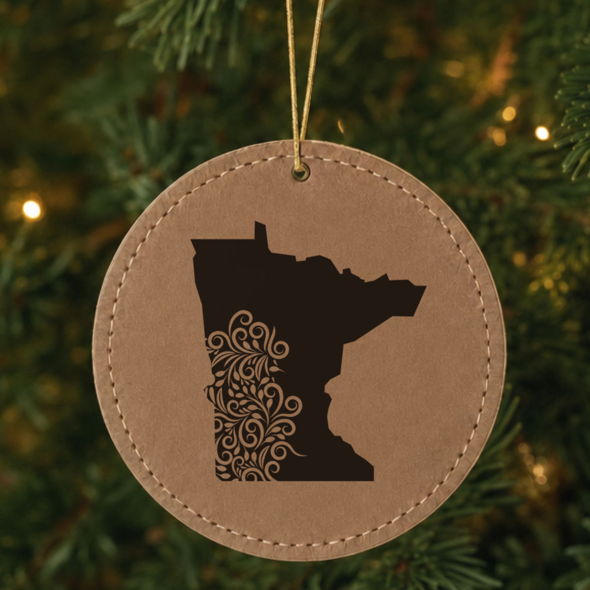 Brown leatherette round Christmas ornament laser engraved with the Minnesota Floral Damask design, hanging on a tree